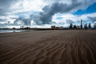 Atlantik Okyanusu 'ndaki büyük Essaouira sahillerinin güzel manzarası. Limanı ve sarı kumuyla mavi gökyüzü Fas' ta beyaz bulutlarla benekli.