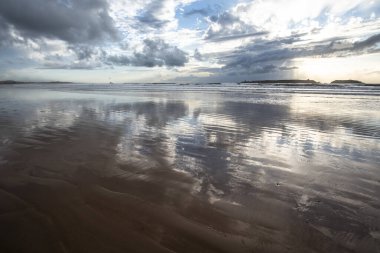 Atlantik Okyanusu 'ndaki büyük Essaouira sahillerinin güzel manzarası. Limanı ve sarı kumuyla mavi gökyüzü Fas' ta beyaz bulutlarla benekli.