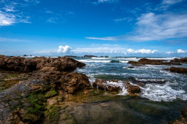 Essaouira şehrinin etrafındaki kayalar Fas şehrini mavi gökyüzü ve beyaz bulutlar arasındaki Atlantik Okyanusu 'ndan korur.