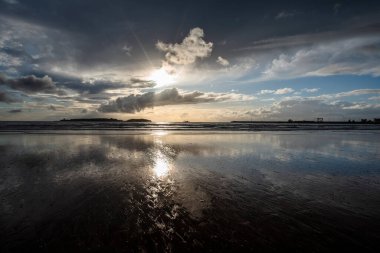 Beyaz bulutlu mavi gökyüzü ve Essaouira limanı yazın günbatımında kumsallarının kıyılarına yansıyor.