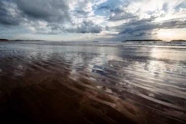 Essaouira 'nın engin sahillerinde gün batımında mavi gökyüzü, beyaz bulutlar ve dalgalar Fas kıyılarına çarpıyor.