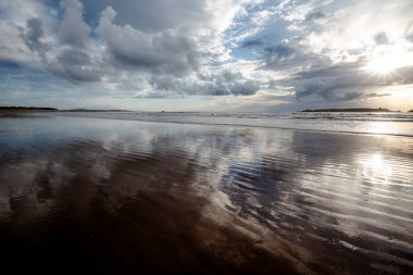 Essaouira 'nın engin sahillerinde gün batımında mavi gökyüzü, beyaz bulutlar ve dalgalar Fas kıyılarına çarpıyor.