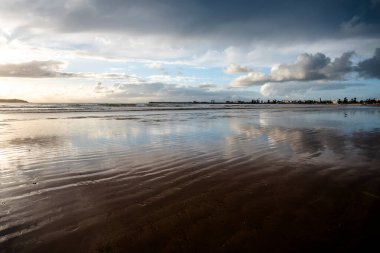 Essaouira 'nın engin sahillerinde gün batımında mavi gökyüzü, beyaz bulutlar ve dalgalar Fas kıyılarına çarpıyor.
