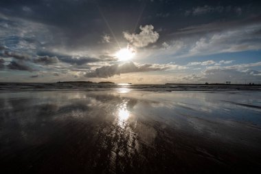 Essaouira 'nın engin sahillerinde gün batımında mavi gökyüzü, beyaz bulutlar ve dalgalar Fas kıyılarına çarpıyor.