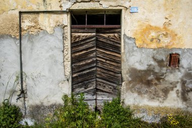 Yıpranmış ringa kemiği tahtaları olan eski ahşap kapı ufalanan alçı duvarda. Kırsal dokular, eski boyalar ve doğal çürüme doğal gün ışığında klasik bir kırsal atmosfer yaratır..