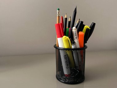 Kalemler, fosforlu kalemler ve kalemler bir kalem tutacağında. Ofis masasında ayrı bir nesne var..