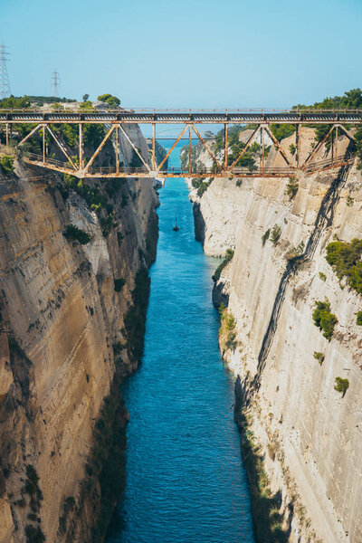 Коринфский канал. На фото старый мост через Коринфский канал и вдалеке корабль, плывущий по каналу. Канал глубокий и построен в скале. Вода в канале темно-синяя..