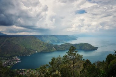 Bu panoramik fotoğraf, Endonezya 'daki Sumatra' da bulunan Toba Gölü 'nün nefes kesici güzelliğini yakalar. Görüntülerde geniş göl, yemyeşil tepeler ve dramatik bir gökyüzü altında dağlarla çevrili., 