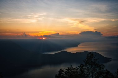 Toba Gölü üzerinde Altın Gün Doğumu bu büyüleyici fotoğraf Sumatra, Endonezya 'da Toba Gölü üzerinde altın bir gündoğumu görüntüler. Sakin sular ve bereketli tepeler, nefes kesici bir manzara arayan doğa ve seyahat meraklıları için mükemmel sakin bir manzara yaratır..