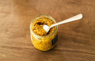 Open jar of french whole-grain yellow mustard with a spoon inside - top view