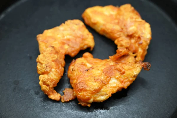 three pieces of white meat fried in batter on cast iron frying pan