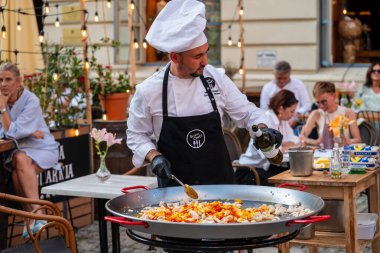 Lublin, Polonya, 26 Temmuz 2024 Sokakta şef Şık bir restoranın önünde süslü bir tabakla büyük bir tavaya şarap döküyor