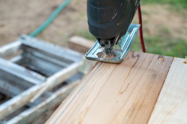 Amatör bir marangoz yapbozla tahta kesiyor. Karşılıklı bir bıçakla bir çeşit elektrikli alet.