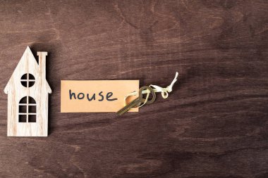 Ahşap ev temsilciliği ve üzerinde ev kelimesi yazan anahtarlık. Ev alıp satma konsepti.