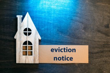 wooden cut out house representation on a wooden table with a card saying 'eviction notice' lit by dramatic blue light clipart