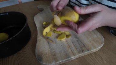 Kadın eli bıçakla patates soyar.