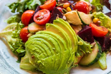 Avokado kiraz domatesli karışık salata salatalık pancar kökü ve yeşil salata yaprakları tabakta.