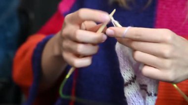 young woman using white and violet yarn and bamboo knitting needles to knit a scarf