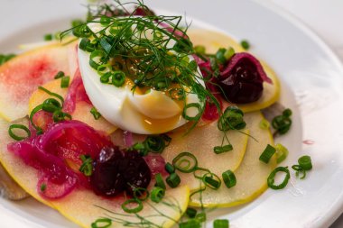 Bir restoranda armut ve terbiye edilmiş kırmızı soğan salatasıyla servis edilen haşlanmış yumurta.