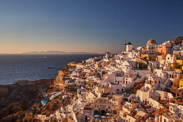 Beautiful view from the old castle of Oia village with traditional white houses and windmills in Santorini island in Aegean sea at sunset, Greece