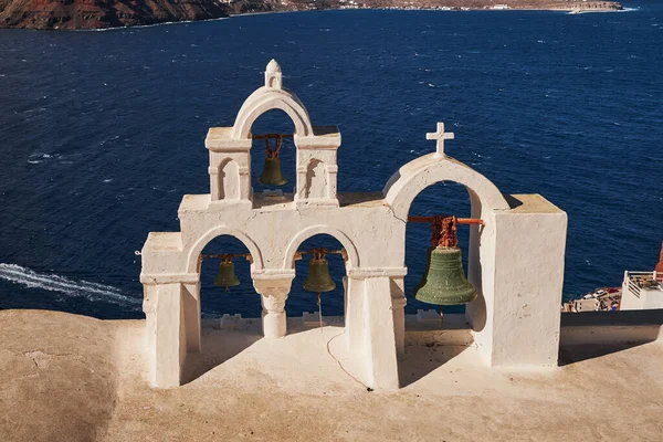 White Bell Tower of an orthodox Church and Greek Flag - Oia Village in Santorini Island, Greece - Sunset