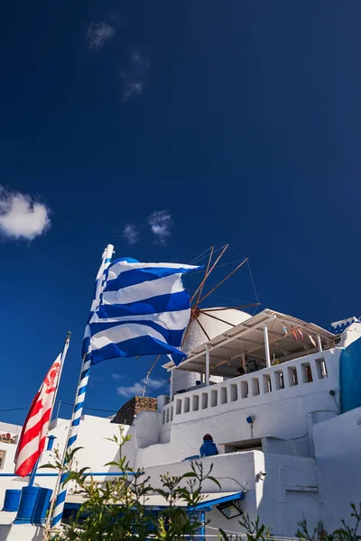 White Bell Tower of an orthodox Church and Greek Flag - Oia Village in Santorini Island, Greece - Sunset