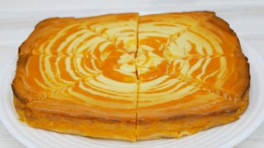 Cottage cheese casserole with pumpkin in a white plate on a white wooden table. Striped casserole with cheese and pumpkin. Cheese pumpkin cake. Cheesecake