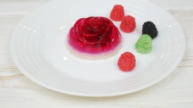 Rose shaped jelly dessert made from raspberries and cream in a white plate on a white wooden table. Decorative red, black and green raspberries