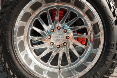 Parlak krom kenarlı kamyonet tekerleği, arka planda ve off-road lastiğinde kırmızı süspansiyon görünür..