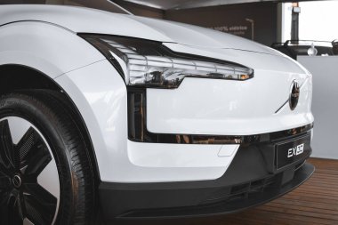 Modern tasarımı ve stilize LED farları olan beyaz bir Volvo EX30 SUV 'un önünde, zarif ve teknolojik görselliği vurguluyor..