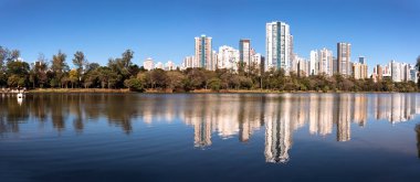 Önünde bir göl olan şehir manzarası ortada bir bitki örtüsü ve arka planda yerleşim yerleri olan gökdelenler.