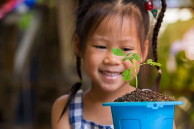 Şirin çocuklar mavi çaydanlıktaki yeşil filizlere aşkla bakar. Mutlu bir gülümseme ve bir saksıya yerleştirilmiş kaçış.