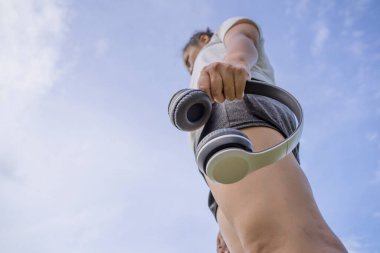 Mavi arka planda beyaz kulaklık tutan Asyalı genç bir kadın..