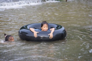 Chiang Mai, Tayland 'da çekilen suda yüzen bir lastik üzerinde oynayan ve yatan bir çocuk..