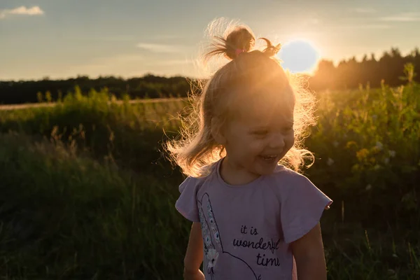 stock image little girl laughs cheerfully in the middle of the field in the backlight at sunset in the summer time