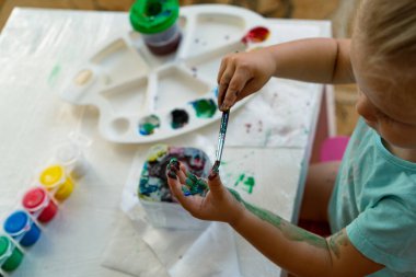 Bir çocuk elini fırçayla boyuyor, yakın plan.