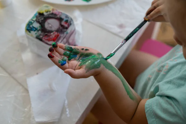 a child paints his hand with colored paints with a brush, close-up