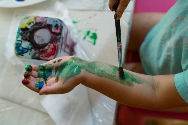 a child paints his hand with colored paints with a brush, close-up