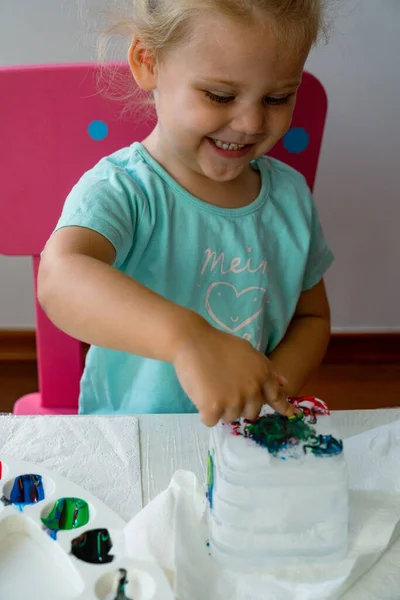little girl paints an ice castle with colored paints and she is very happy with the process of painting a girl in a blue t-shirt with the inscription \