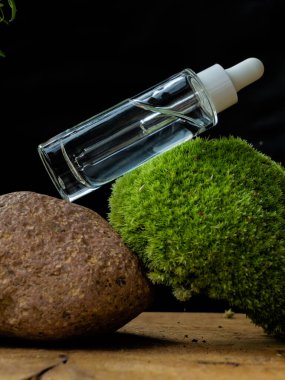 glass transparent bottle with natural cosmetic product and dispenser on moss, stone, tree and black background