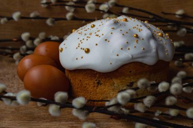 Beyaz kremalı Paskalya ekmeği ahşap bir arka planda yumurtalı ve söğüt dallı bir yuvada