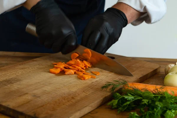 stock image Close-up of a chef's hands in black gloves cutting carrots on a wooden board