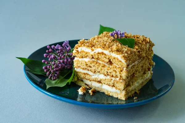 A piece of honey cake on a plate with lilac flowers.