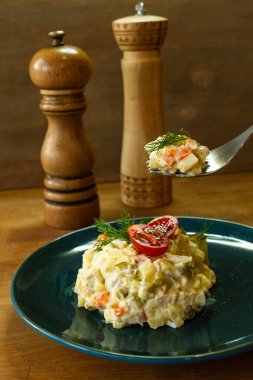 Lezzetli bir Olivier salatası mavi bir tabakta servis edilir. Ahşap arkaplan.