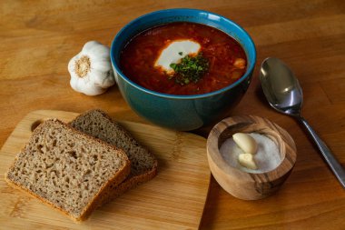 Bir kase sarımsaklı çorba ve ahşap masada ekmek.