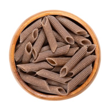 Buckwheat penne, gluten free whole grain pasta, in a wooden bowl. Dark brown noodles, made of pure buckwheat semolina, extruded into cylinder-shaped pieces, their ends cut at an angle, then dried. clipart