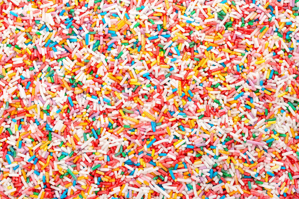 Rainbow sprinkles, background and surface. Rod-shaped colorful sugar sprinkles. Tiny candies in a variety of colors, used as sweet decoration and topping for cookies, cakes and ice cream. Food photo.