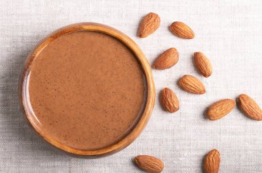 Ahşap bir kasede keten kumaşın üzerinde kahverengi badem yağı. Bademleri öğütüp fındık ezmesine çeviren yumuşak yemek ezmesi. Fındık aromalı erik ezmesi püresi. İyi bir protein kaynağı.