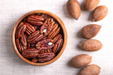 Ahşap bir kasede keten kumaşın üzerinde fındık. Kurumuş ceviz parçaları ve kabuklu cevizler, tohumlar ve Carya illinoinensis fındıkları. Atıştırmalık olarak yemeye hazır ve aynı zamanda pişirmek için de kullanılıyor. Yukarıdan yakın çekim.