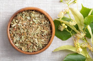 Linden flowers in a wooden bowl on linen fabric. Dried, fresh flowers, fruits and bract leaves of large-leaved linden or lime tree, Tilia platyphyllos. Used for herbal tea and in traditional medicine. clipart